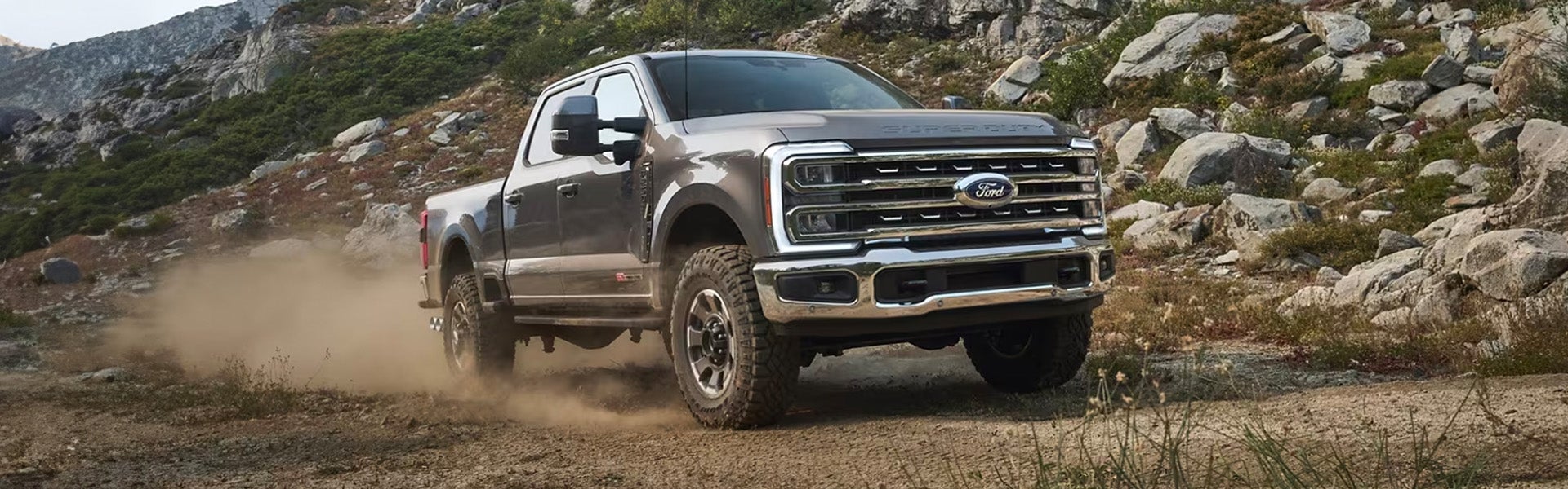 2024 Ford Super Duty driving off-road through a rugged dusty mountain trail