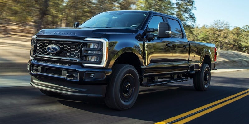 2024 Ford Super Duty in black driving on a highway with trees in the background